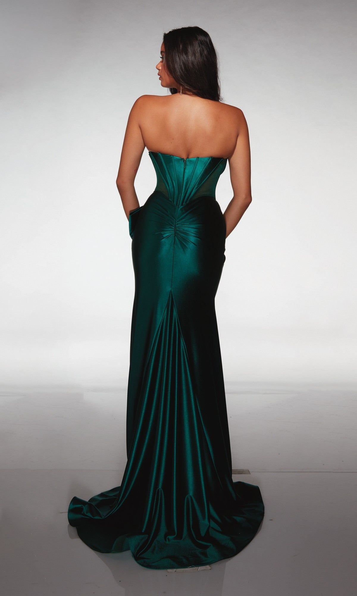 A woman stands with her back to the camera wearing the Alyce 62156, a strapless emerald green satin formal dress featuring a fitted bodice, beaded sweetheart neckline, and long flowing train.